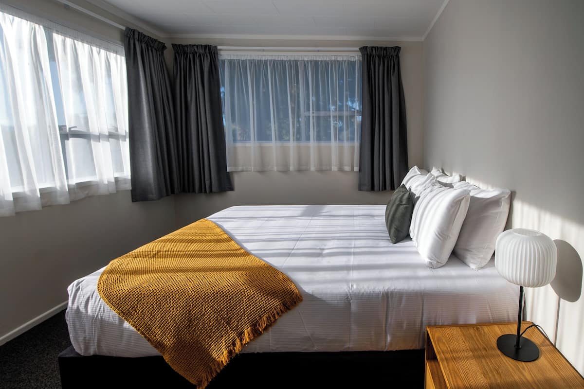 Una habitación de hotel con una cama grande, una mesita de noche de madera y una lámpara.