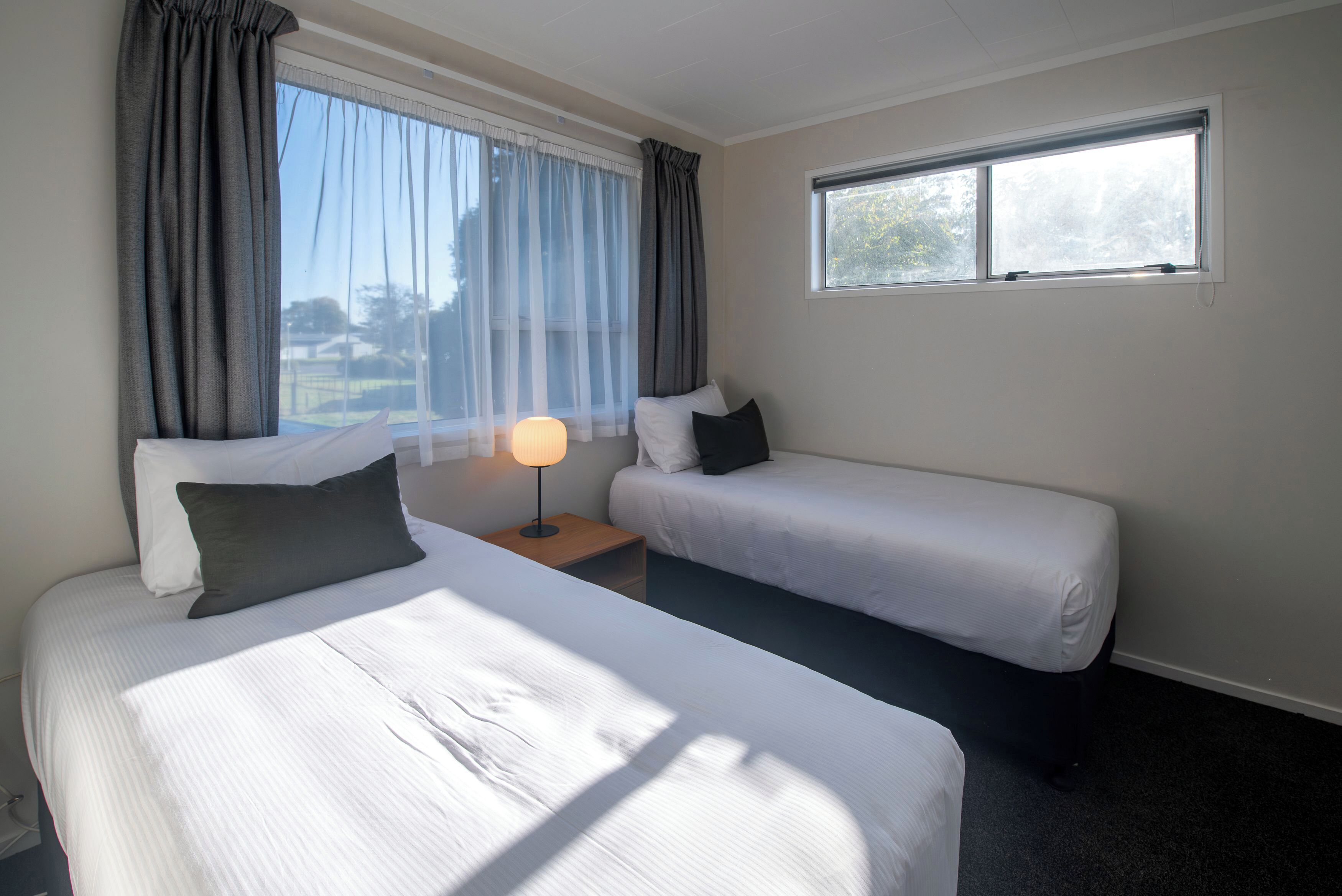 Een hotelkamer met twee bedden, een nachtkastje met een lamp en een raam met gordijnen.