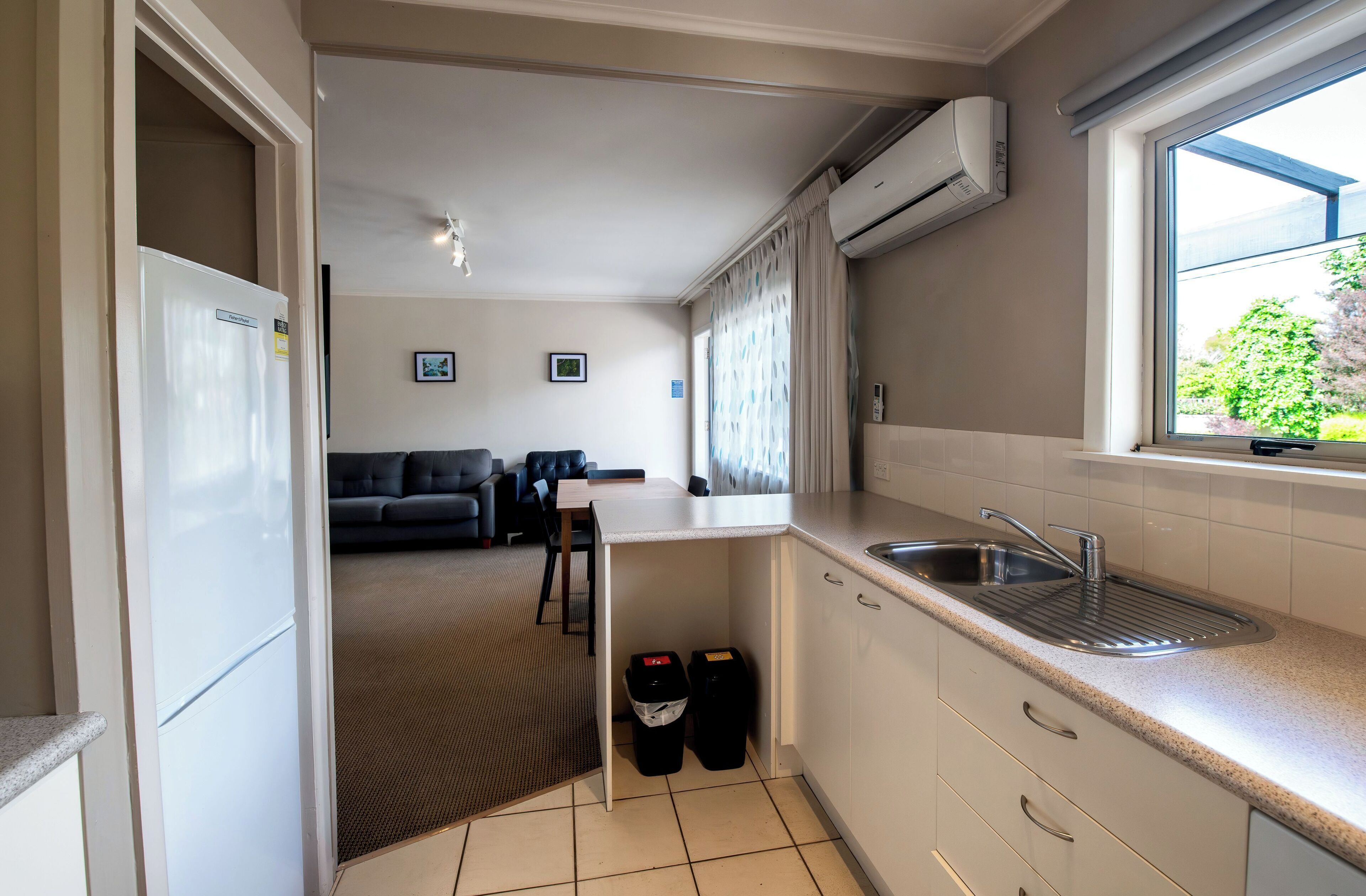 A compact kitchen with a built-in sink, a refrigerator, and a window with curtains.