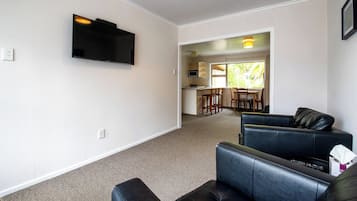 Sala de estar con televisión de pantalla plana montada en la pared, una zona de descanso con sofá y reposapiés, y una cocina con microondas y taburetes de bar.