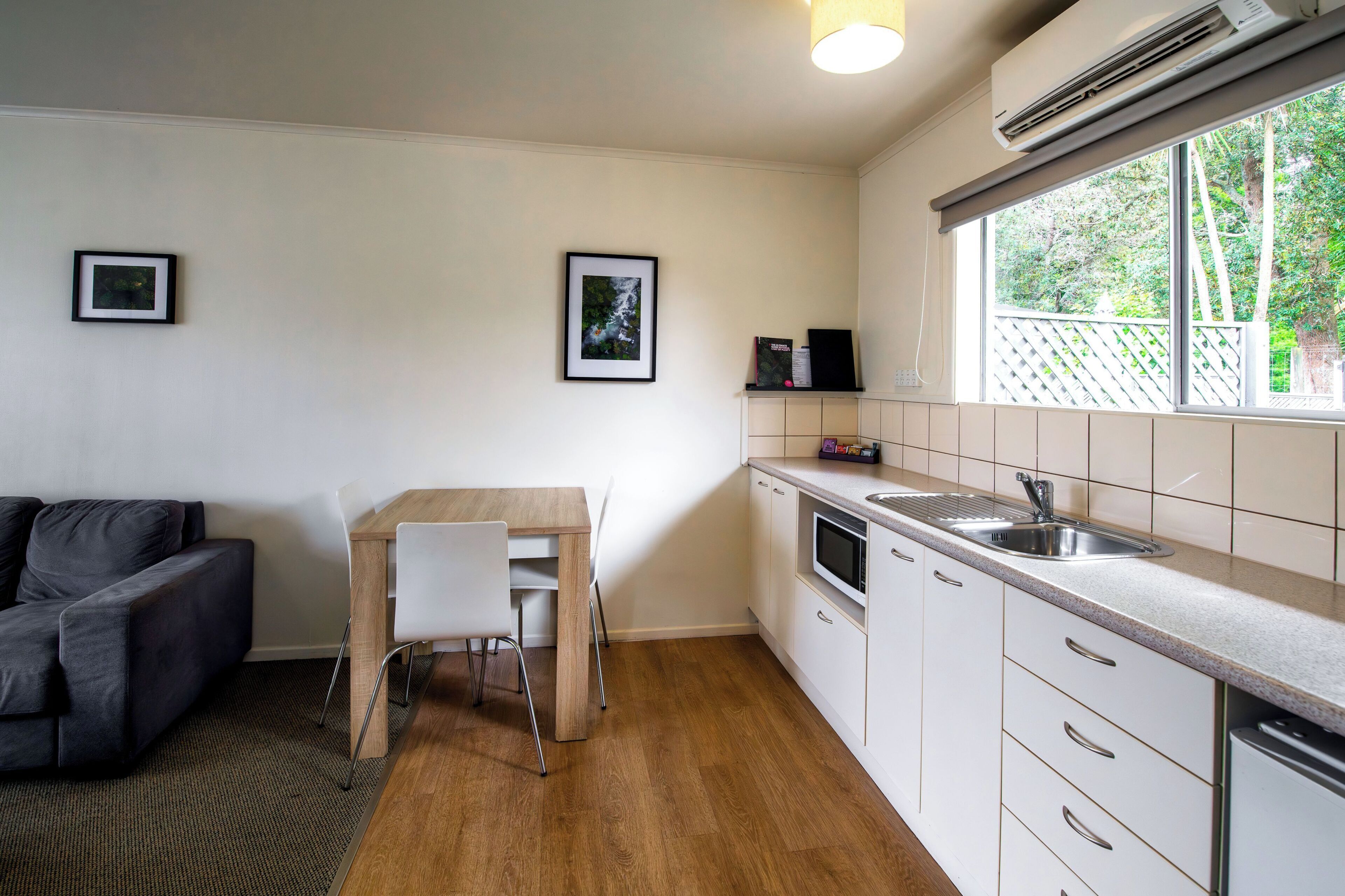 A compact kitchen with a dining table, a built-in microwave, and a window with a view of greenery.