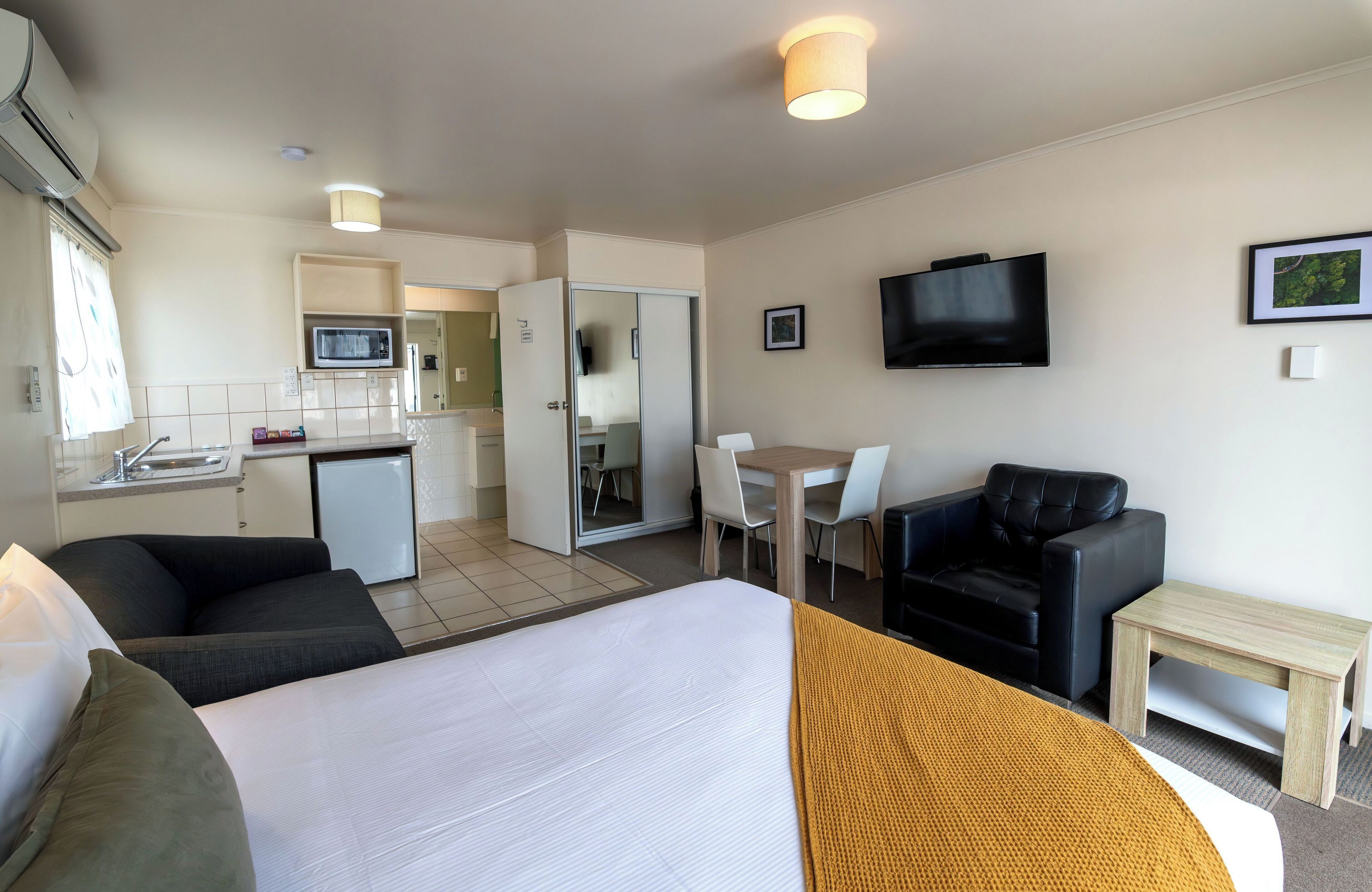 Una habitación de hotel con cama, sofá, televisor, mesa de comedor y kitchenette.