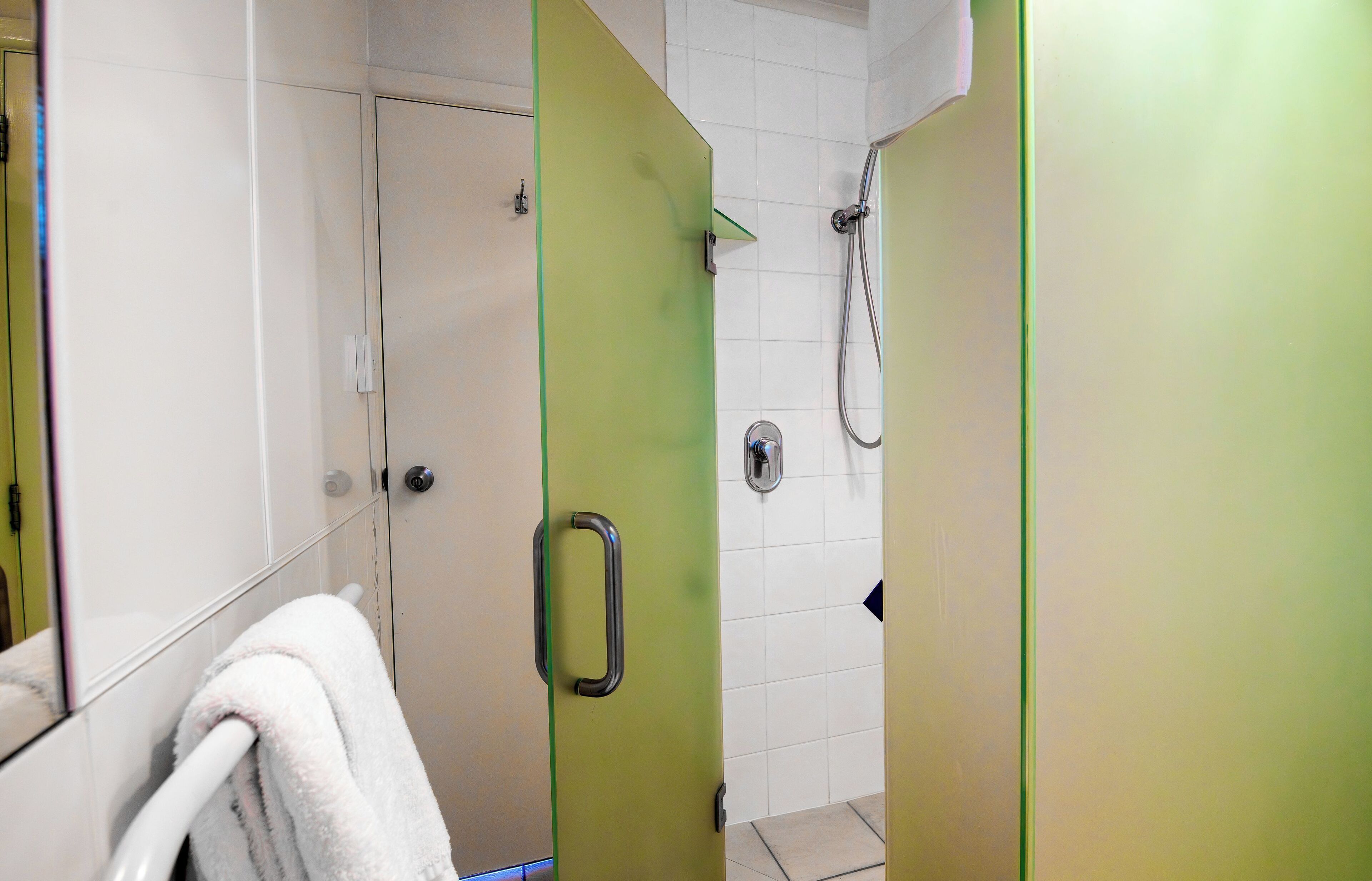 A bathroom with a shower, a towel rack, and a green door.
