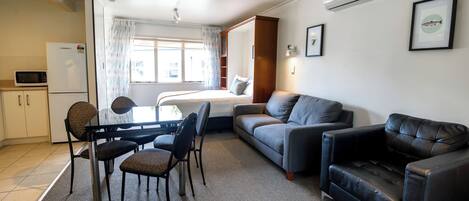 A compact living space with a kitchenette, a bed, a sofa, a dining table with chairs, and a small black leather couch.