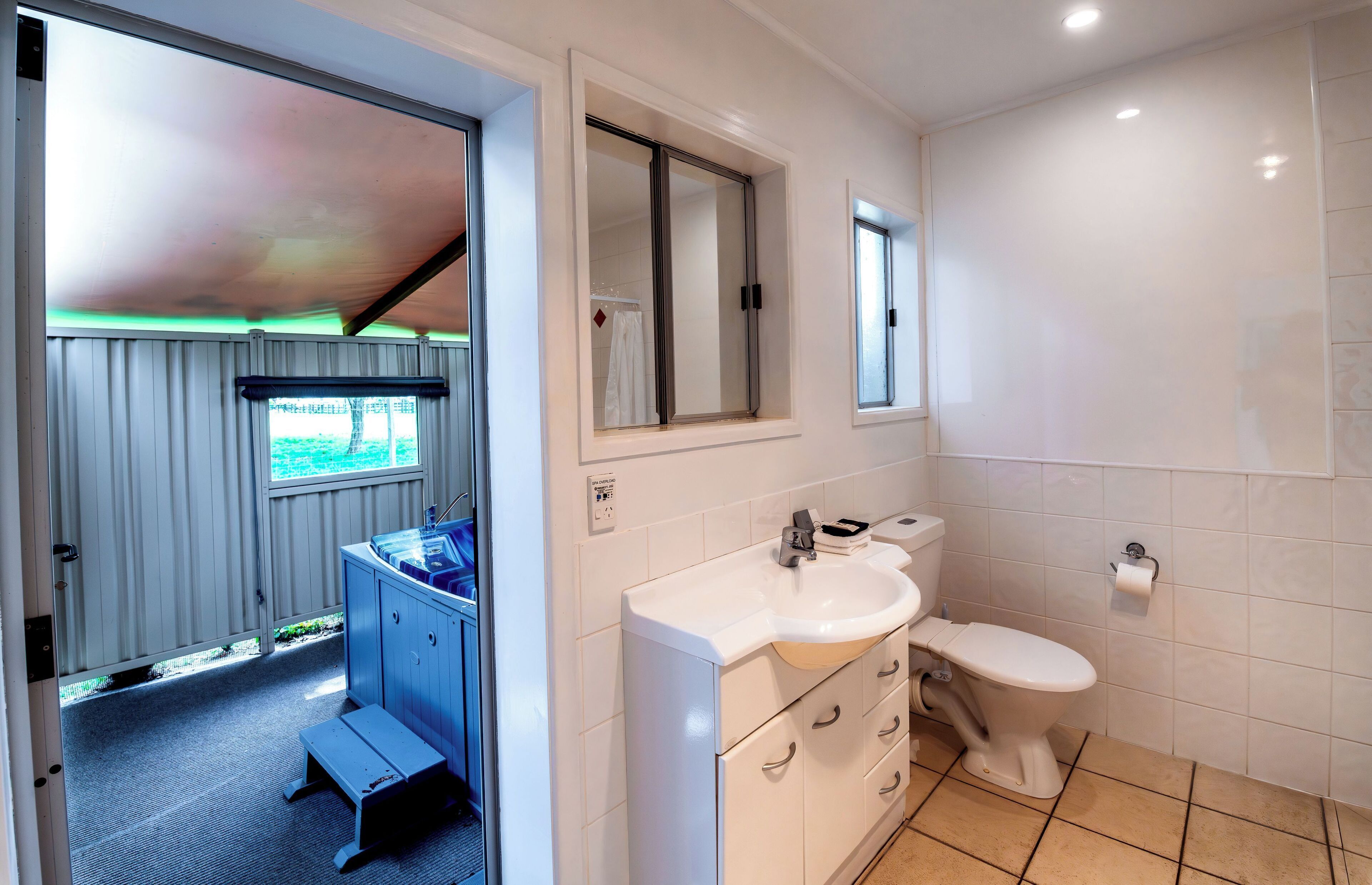A bathroom with a sink, toilet, and a mirror. There is a window with a view of greenery outside.