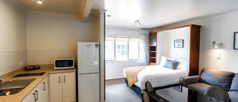 Una habitación de hotel compacta con kitchenette, una cama con cabecera, un sofá y una mesa de comedor.