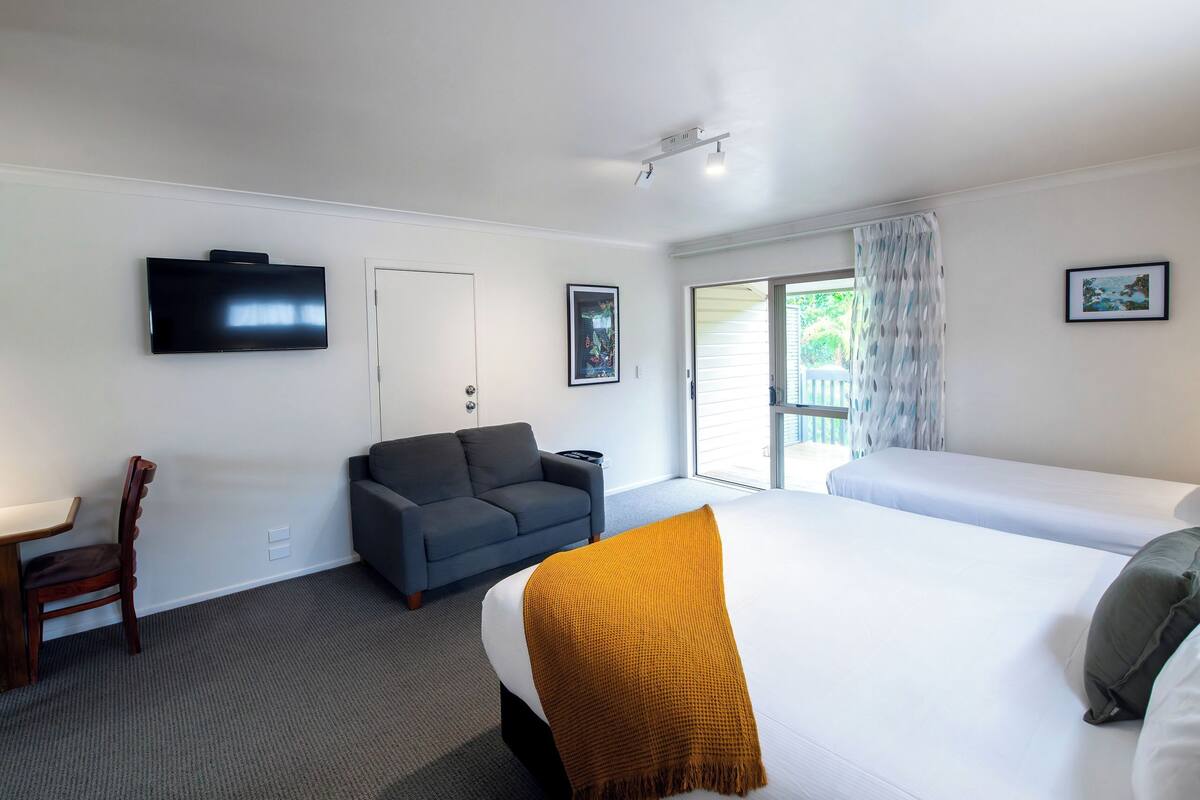 Habitación de hotel con cama, sofá, televisión, escritorio y ventana con cortinas.