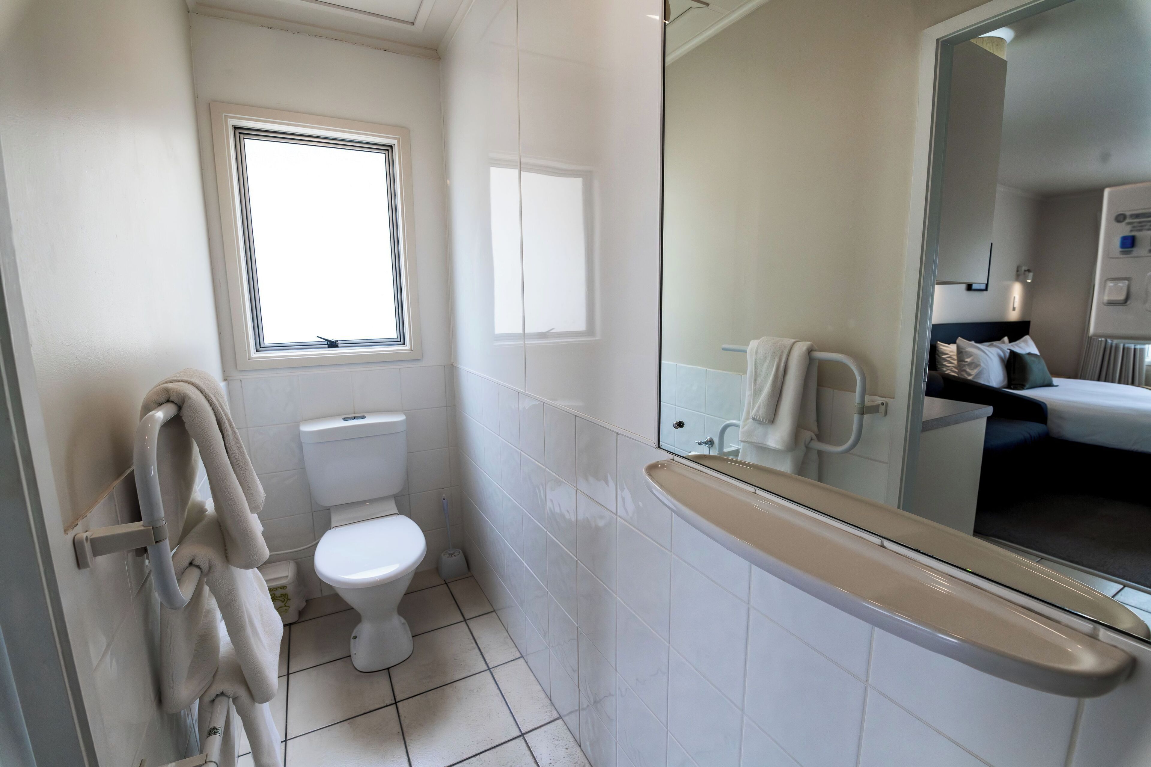 A bathroom with a toilet, a window, a shower area, and a mirror.