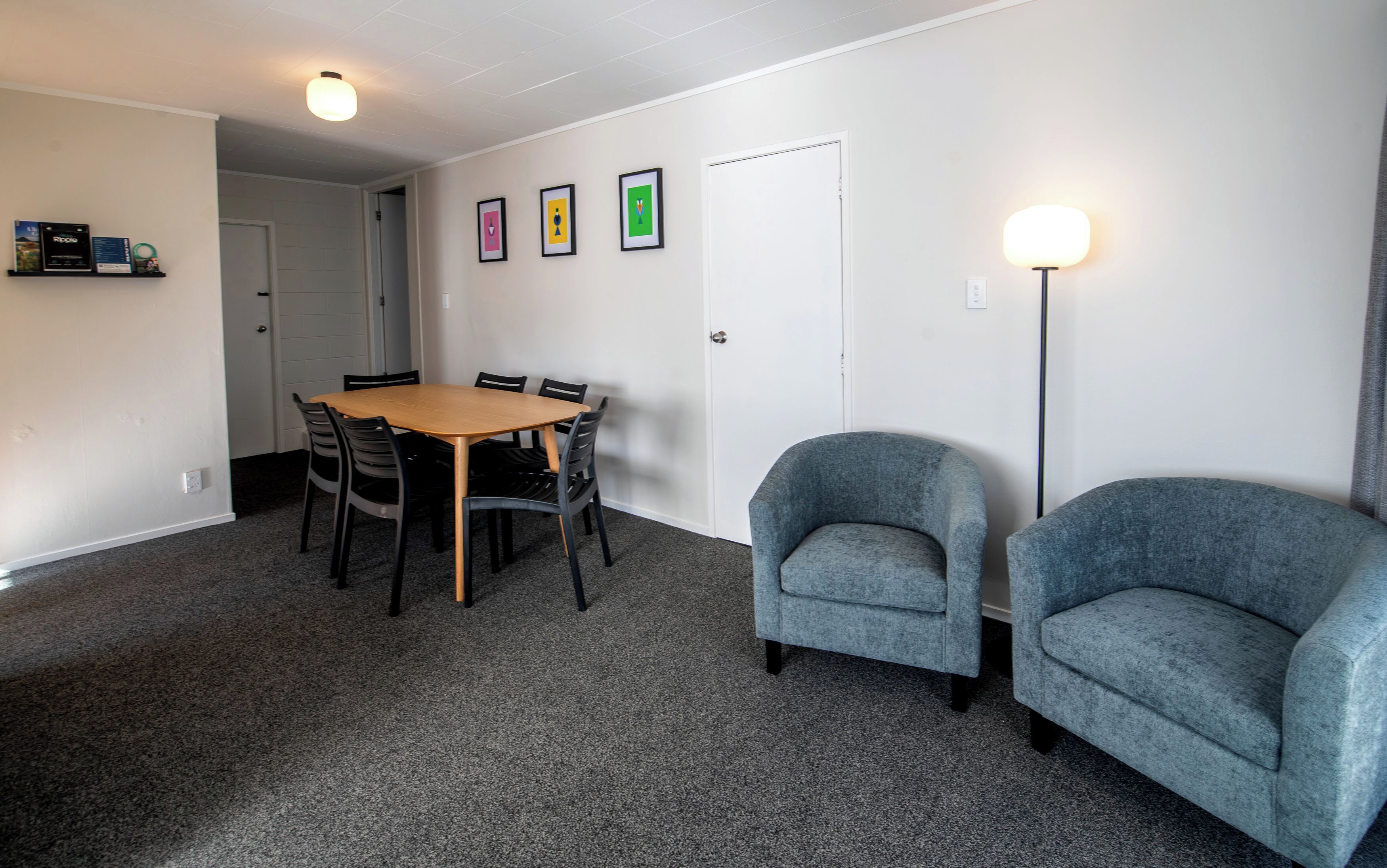 Una habitación con una mesa redonda de madera rodeada de sillas, una puerta y una pared con cuadros enmarcados.