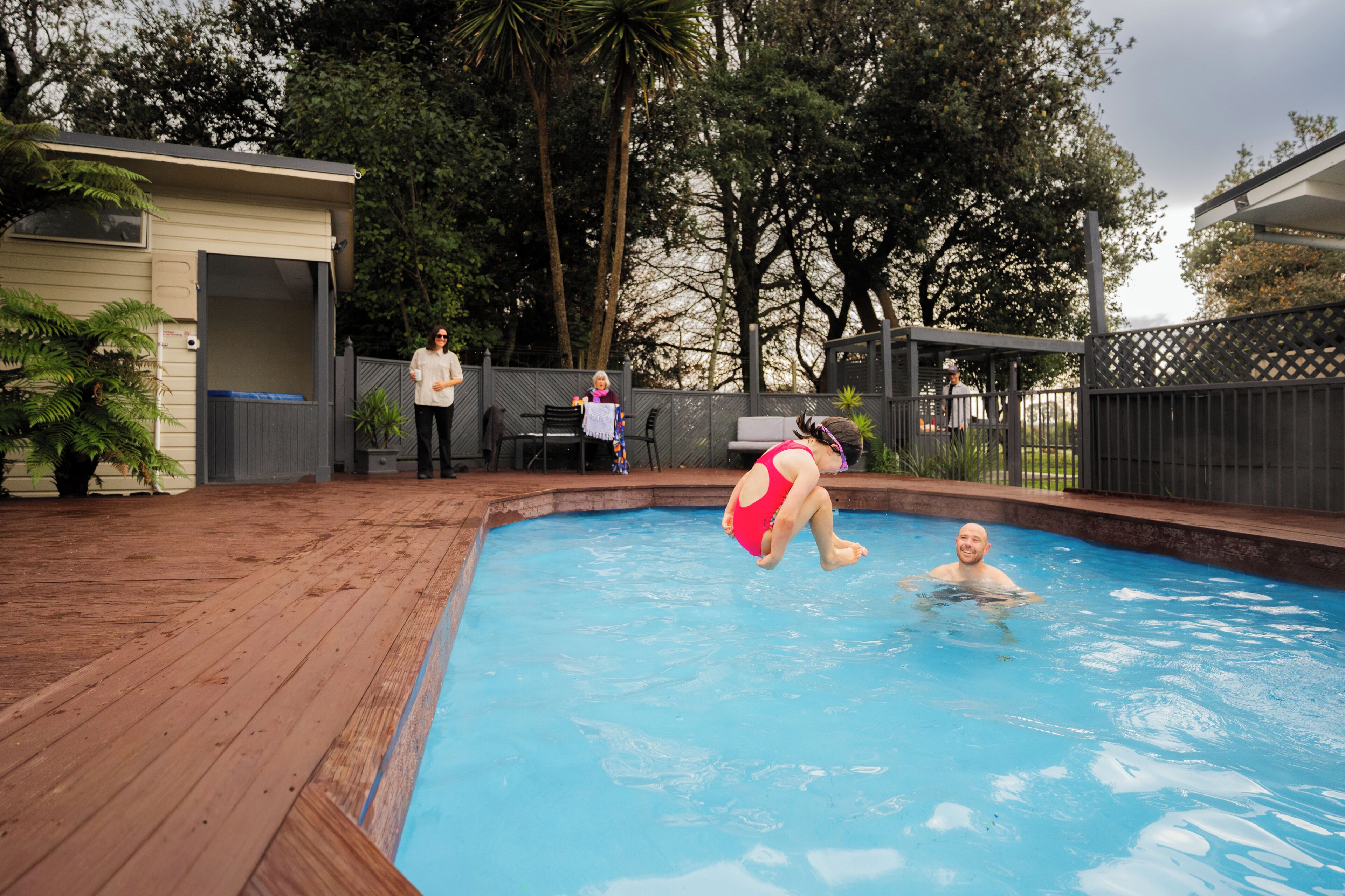 Una piscina con cubierta de madera, rodeada de árboles y una zona vallada.