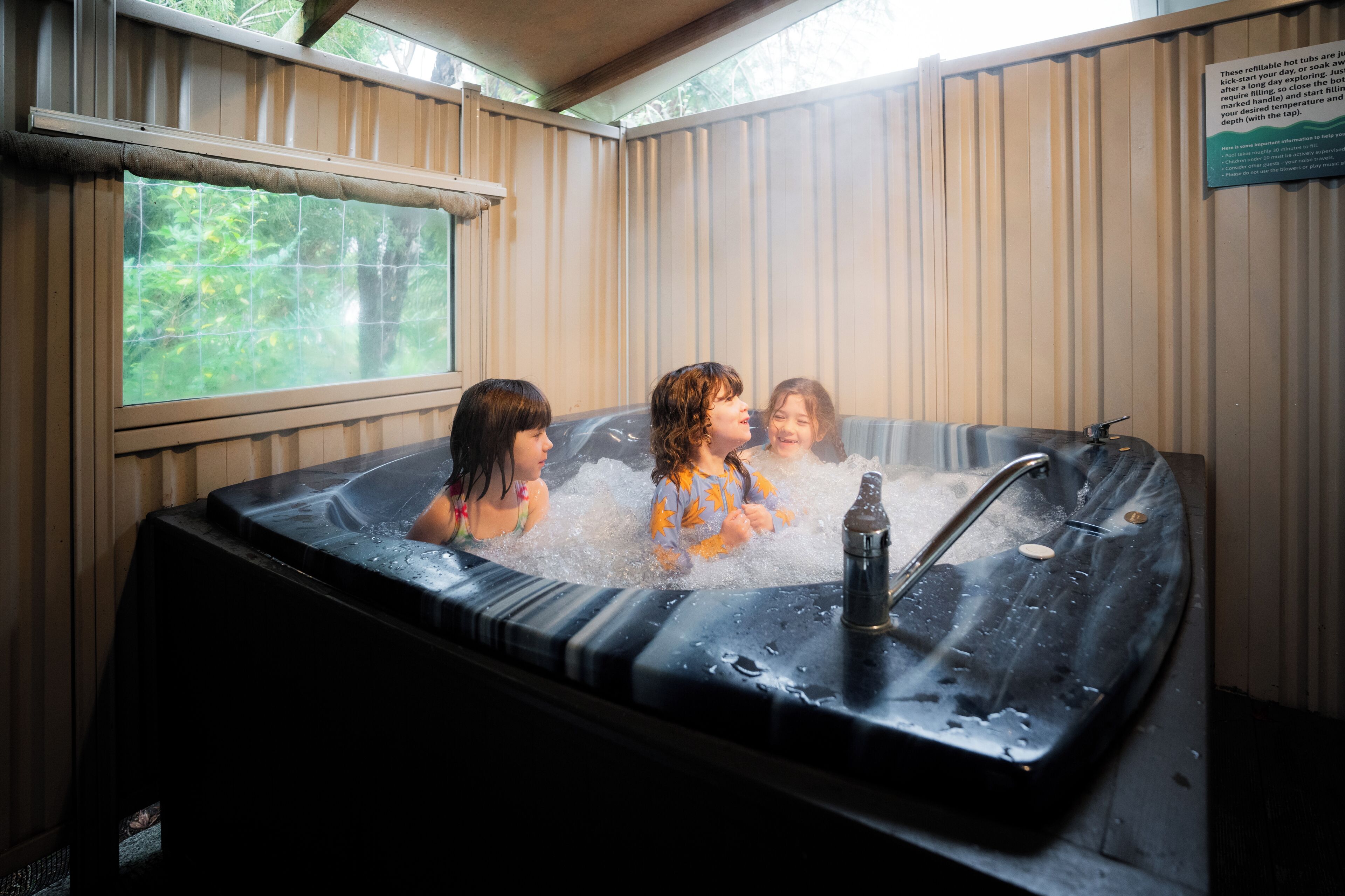 Un jacuzzi con tres personas adentro, rodeado de paredes de madera y un ventanal.