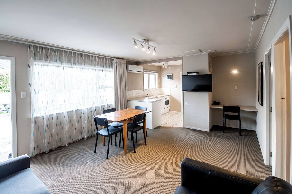Un espacio habitable compacto con comedor, kitchenette y televisor montado en la pared.