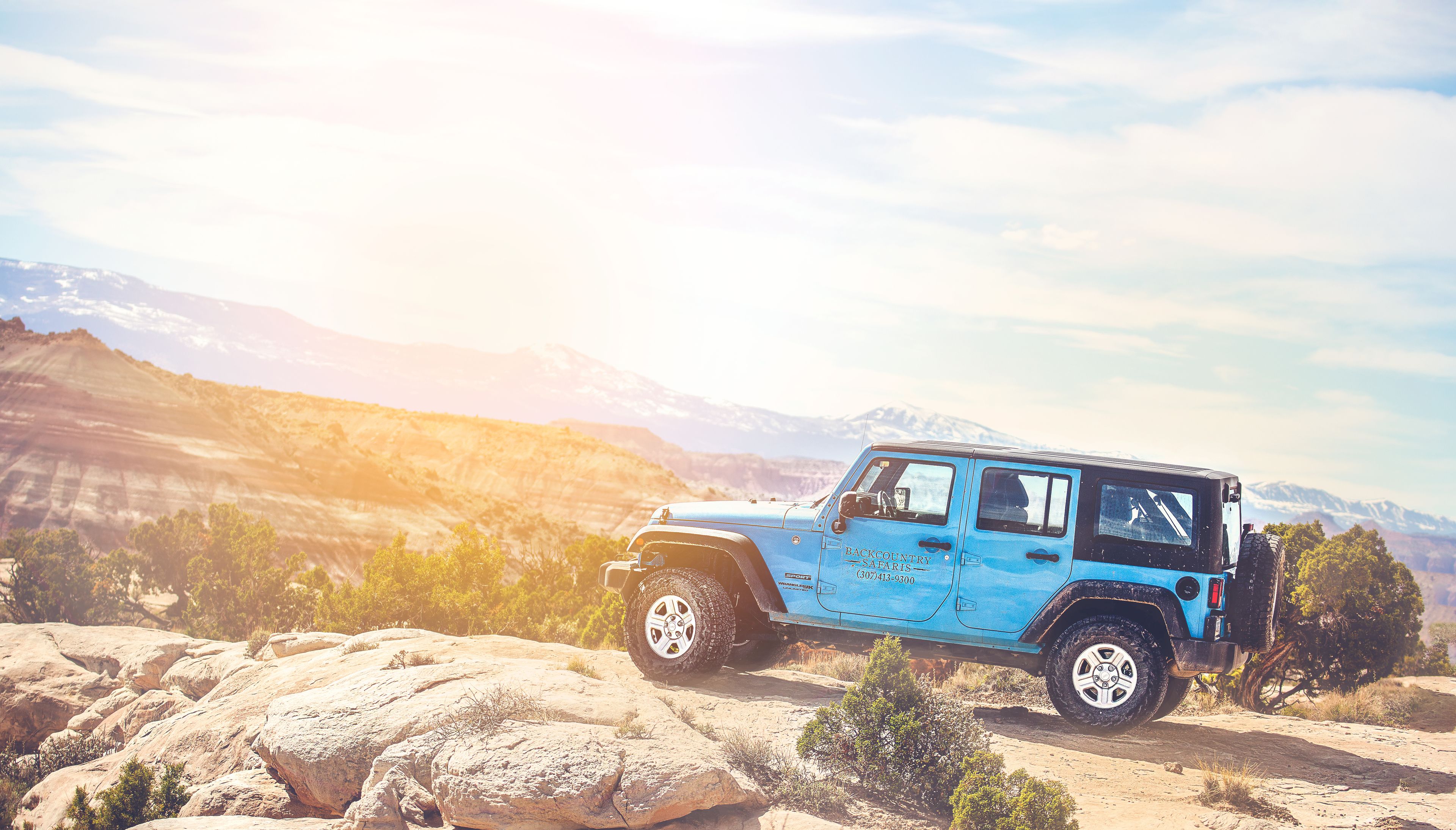 A blue off-road vehicle parked on a rocky terrain with a mountainous backdrop.