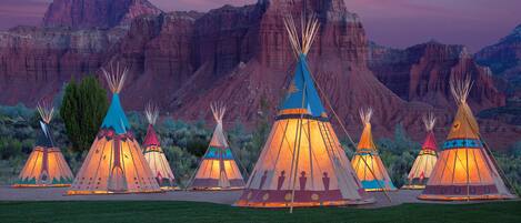 En række traditionelle tipier fra det amerikanske indianerfolk foran et bjergrigt landskab.