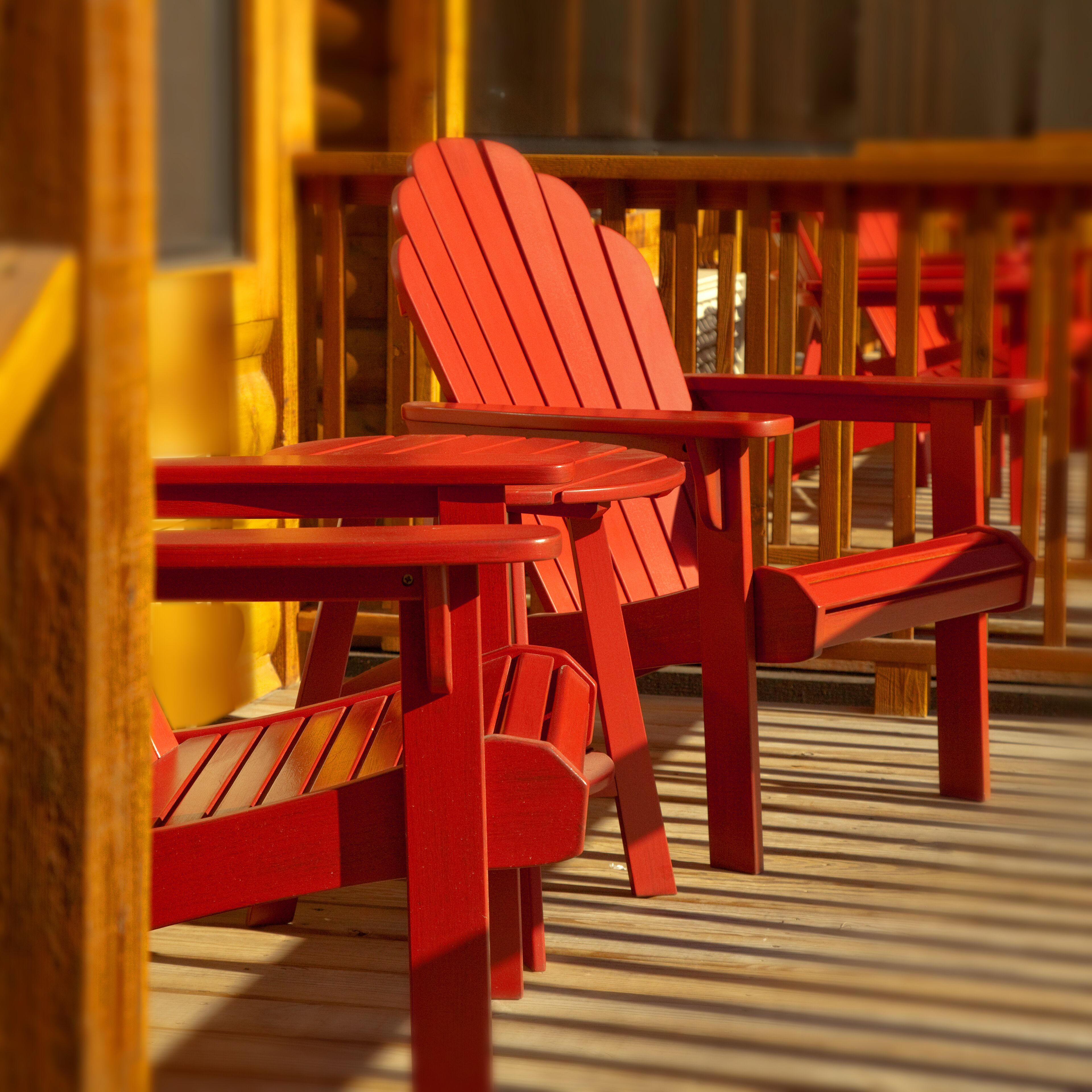 A row of red Adirondack chairs and a wooden table on a wooden deck.