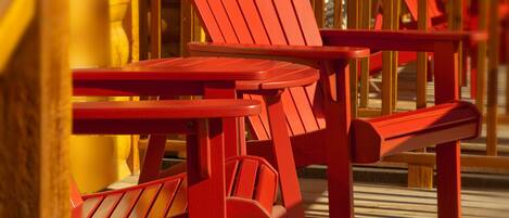 A row of red Adirondack chairs and a wooden table on a wooden deck.