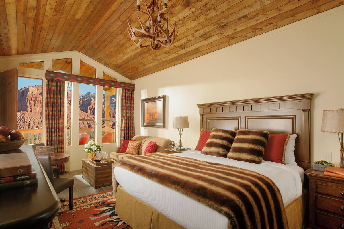 A spacious bedroom with a large bed, a wooden ceiling, a view of a canyon through the window, and a chandelier.