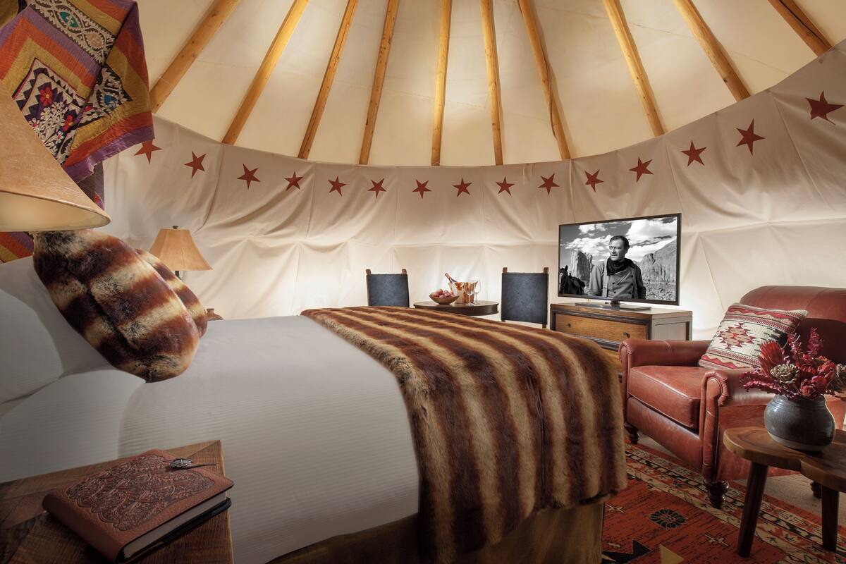 A yurt interior with a bed, a chair, a table, and a television.