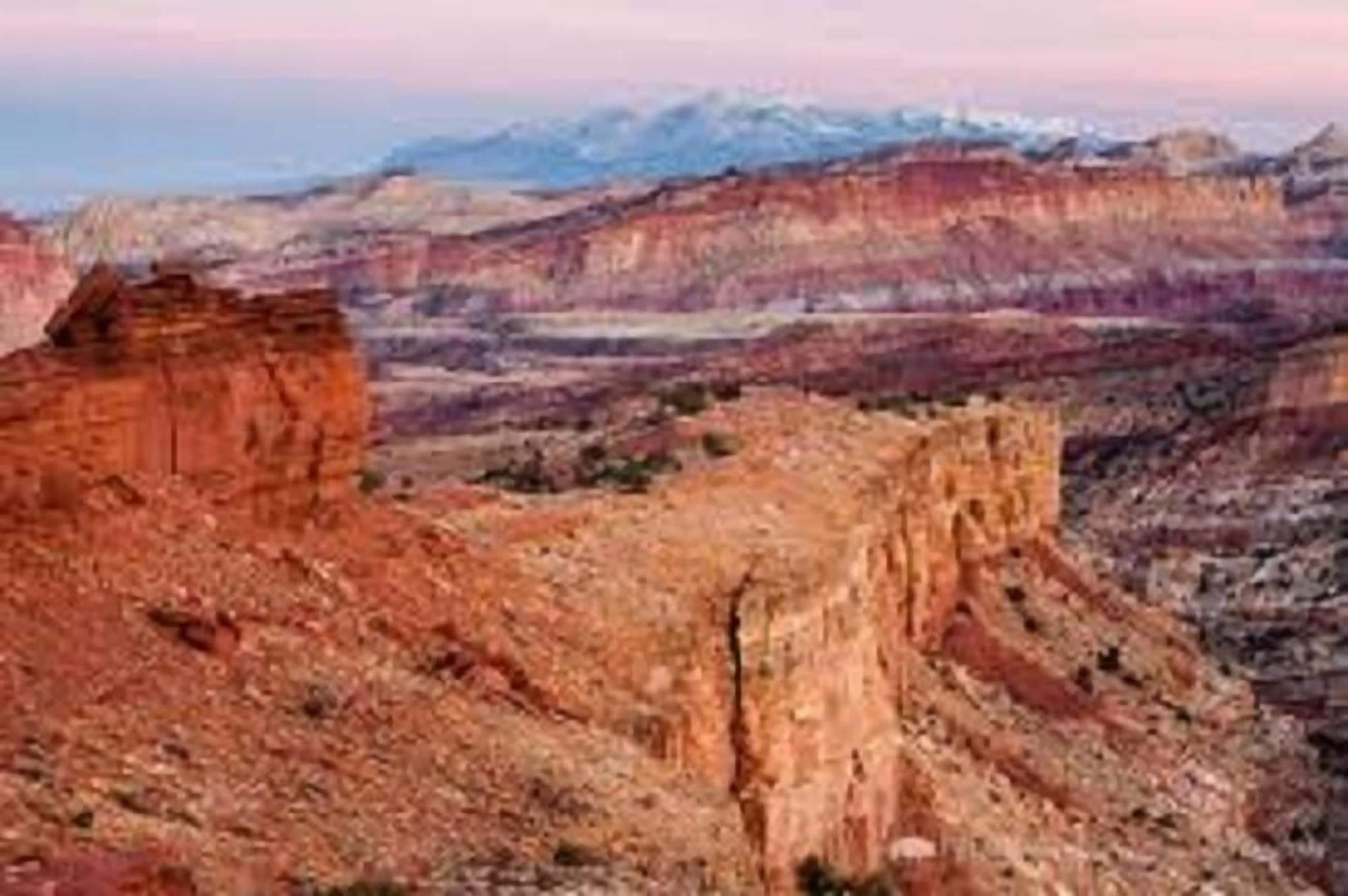 A canyon landscape with layered rock formations and distant snow-capped mountains.