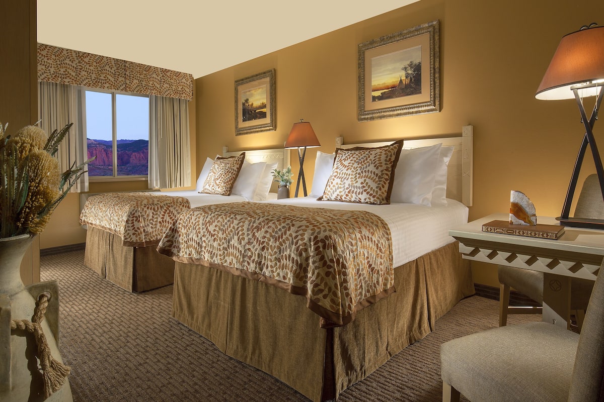 A hotel room with a large bed, two bedside tables, a lamp, and a view of the desert through the window.