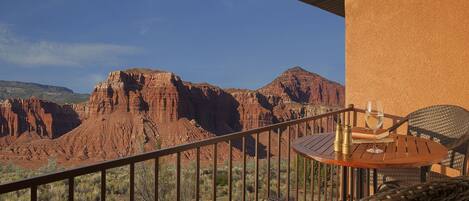 A balcony with a view of red rock formations, a table with a glass of wine, and wicker chairs.