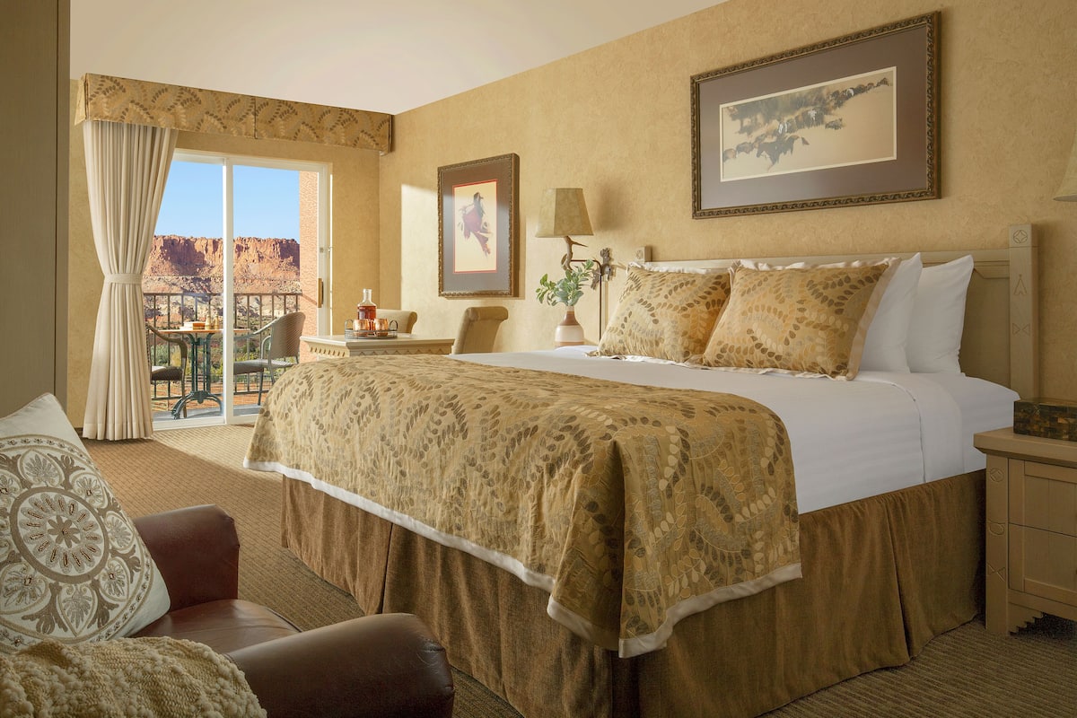 A hotel room with a large bed, a chair, a nightstand, a lamp, and a window with curtains.