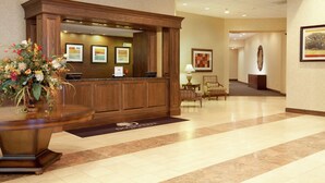 A reception area with a wooden reception desk, a large vase of flowers, framed artwork on the walls, and a carpeted floor. - DoubleTree by Hilton Boston - Milford (Milford)