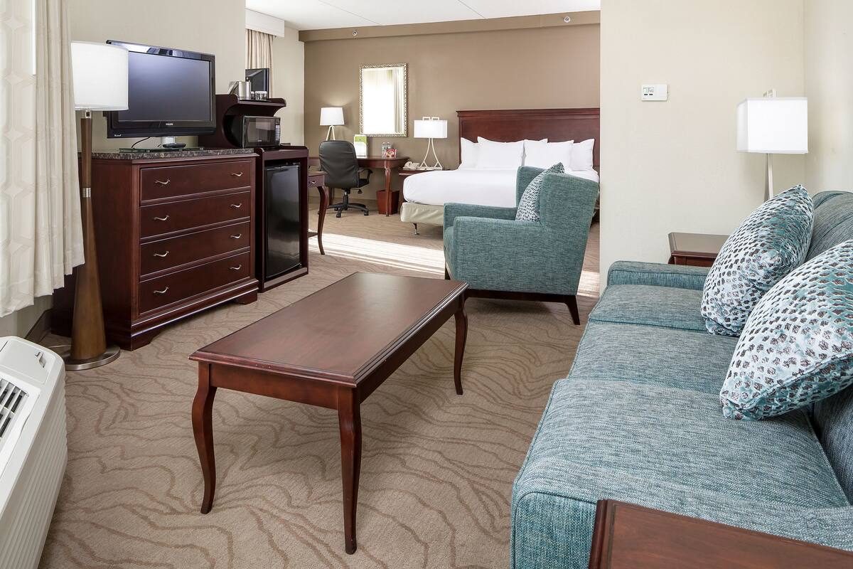 A hotel room with a bed, a sofa, a desk with a computer, a television, and a microwave.