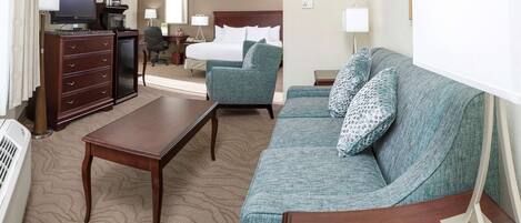 A hotel room with a bed, a sofa, a desk, a television, and a dresser.