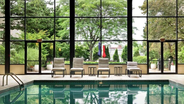 A pool area with a clear view of the surrounding greenery through large windows. - DoubleTree by Hilton Boston - Milford (Milford)