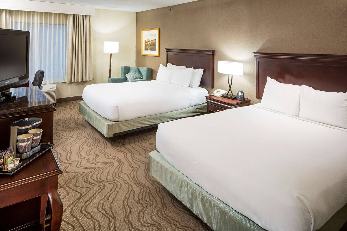 A hotel room with two beds, a desk with a coffee maker, a TV, and a picture on the wall.