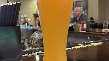 A tall glass of orange juice on a bar counter with a napkin underneath, a black ashtray with cigarettes, and a blurred background of a bar area.