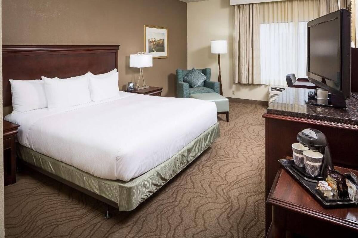 A hotel room with a large bed, a desk with a coffee maker, a television, and a chair.