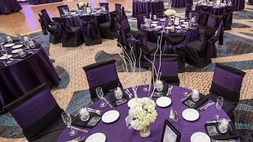A banquet hall with round tables set for a formal event, featuring purple tablecloths and black chairs with purple sashes.