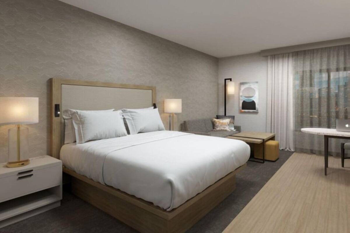 A modern hotel room with a large bed, bedside tables, a desk, and a chair.