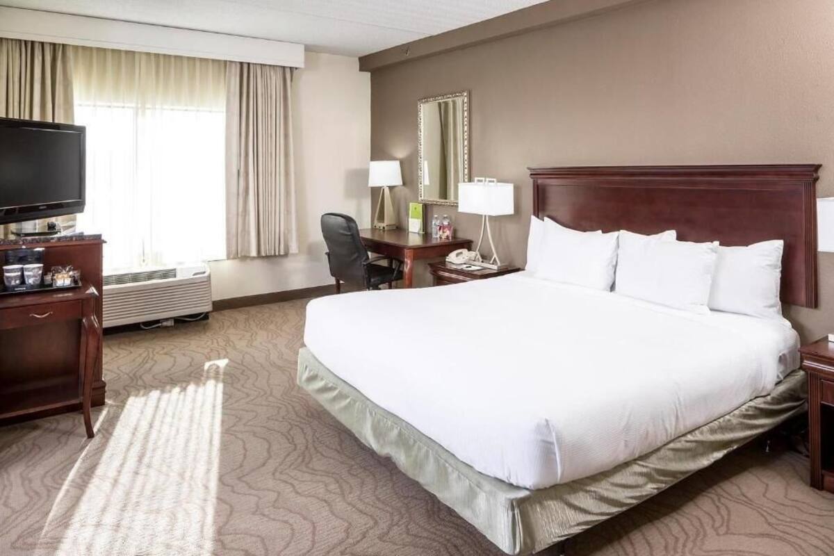 A hotel room with a large bed, a desk with a chair, a television, a mirror, and a window with curtains.