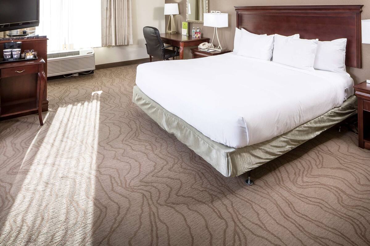 A hotel room with a large bed, a desk with a lamp, a chair, a television, and a mirror.