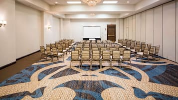 A conference room with rows of chairs, a projector screen, and a carpet with a geometric pattern.