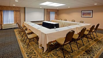 A conference room with a long table, chairs, a projector screen, and a carpeted floor.
