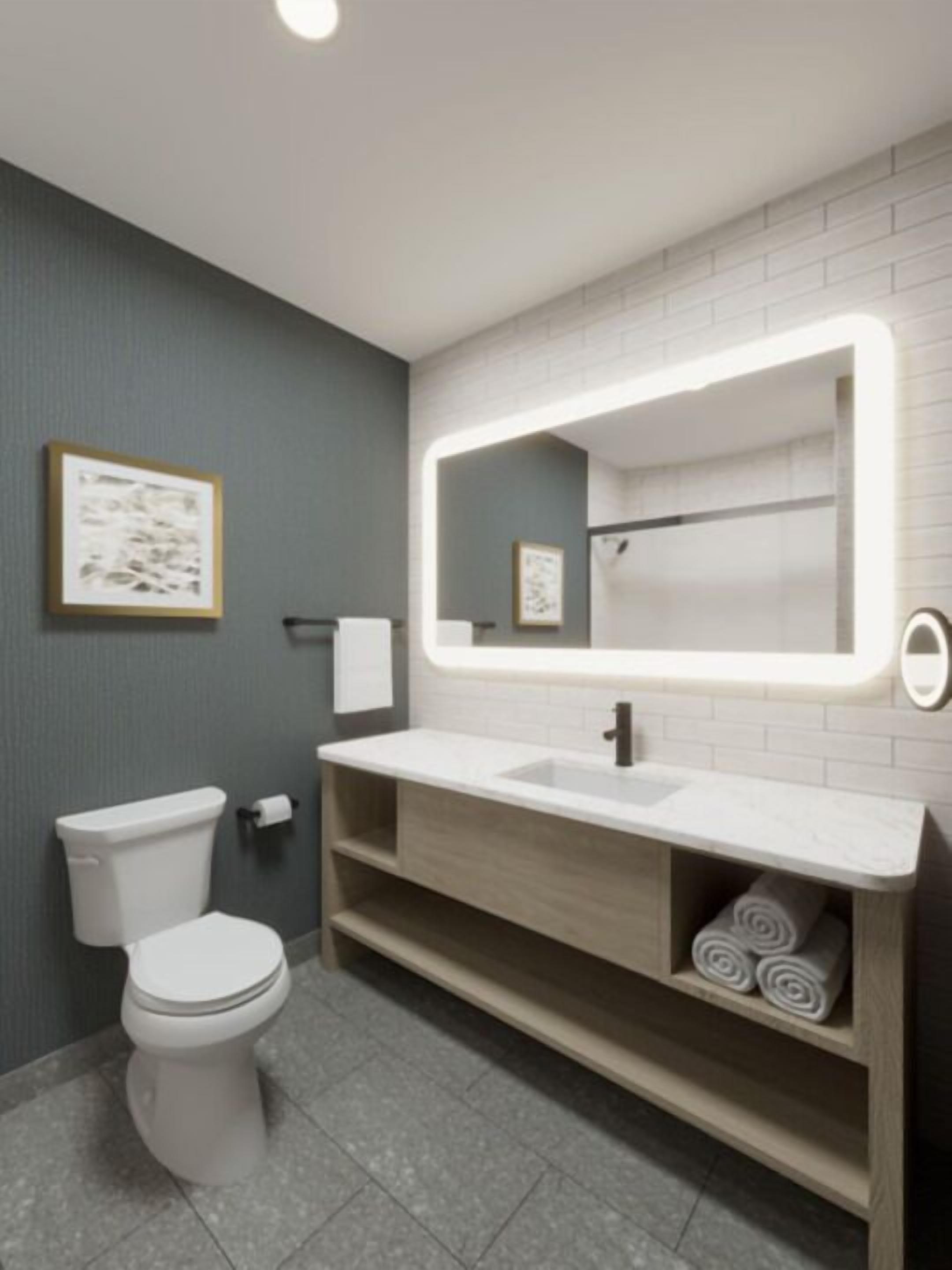 A modern bathroom with a white toilet, a large mirror with LED lighting, and a wooden vanity with a sink.
