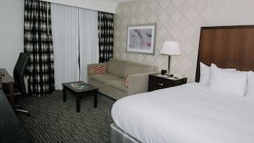 A hotel room with a large bed, a desk, a chair, a nightstand, and a lamp.