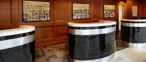A hotel reception area with a wooden panel wall, three trash bins, and framed artwork depicting cityscapes.