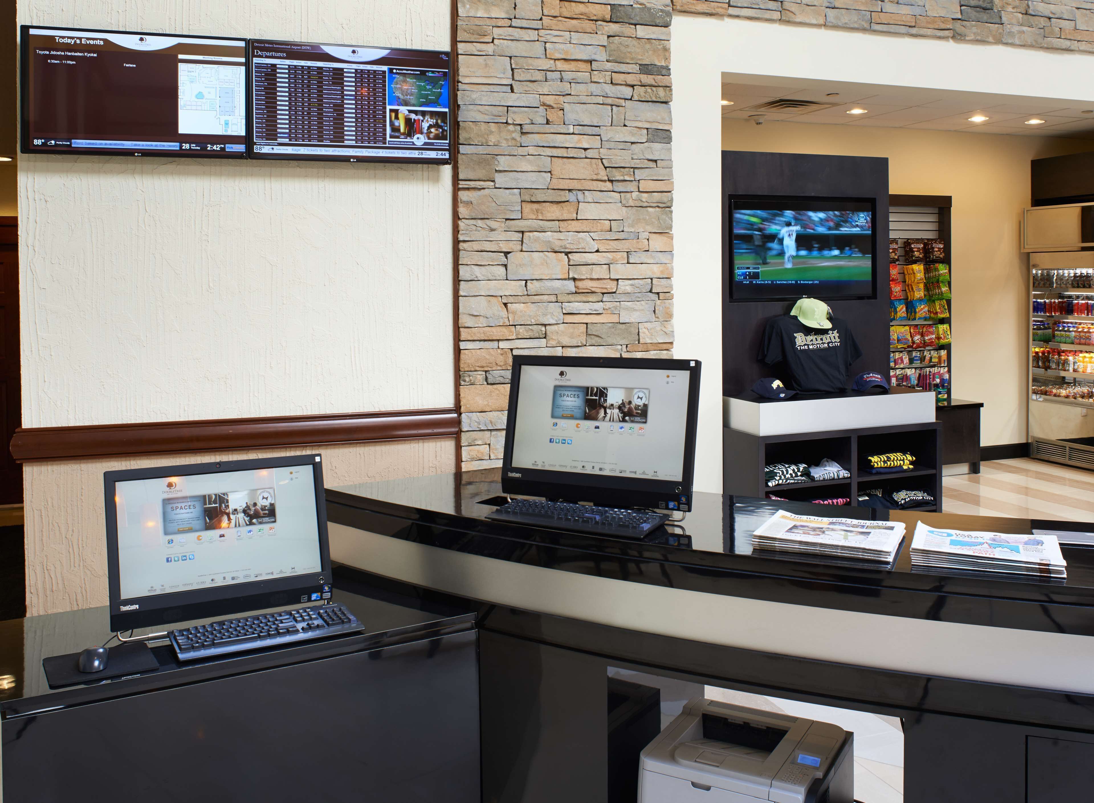 A reception desk with multiple computer monitors, a stone wall, and a vending machine in the background.