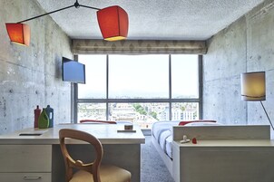 Una camera moderna con una grande finestra, una scrivania, una sedia, un letto e una TV.
