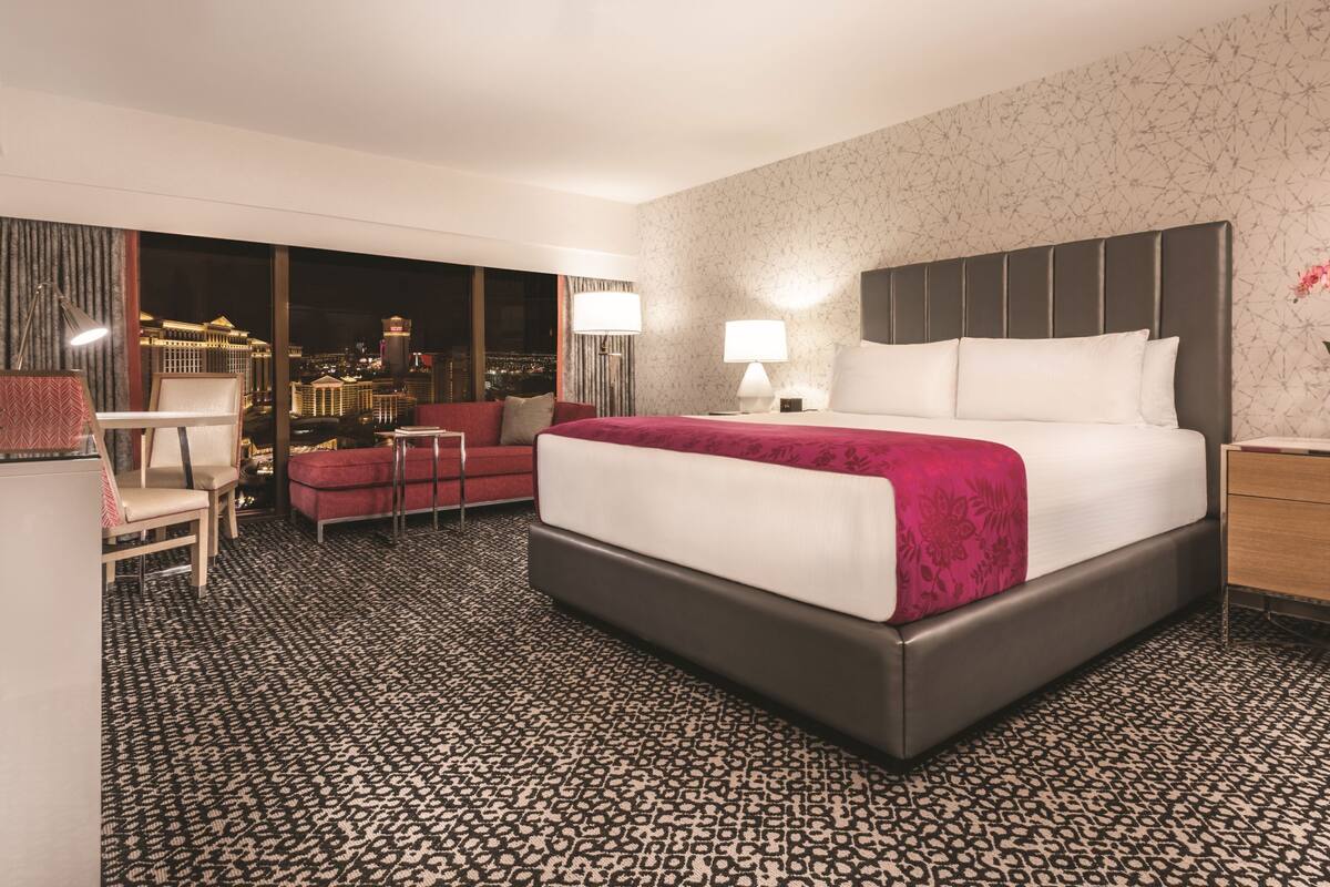 A hotel room with a large bed, a desk, a chair, and a view of a cityscape.