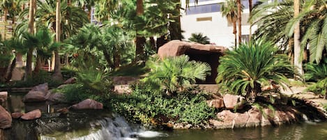 A lush garden with a waterfall, palm trees, and a large rock formation.