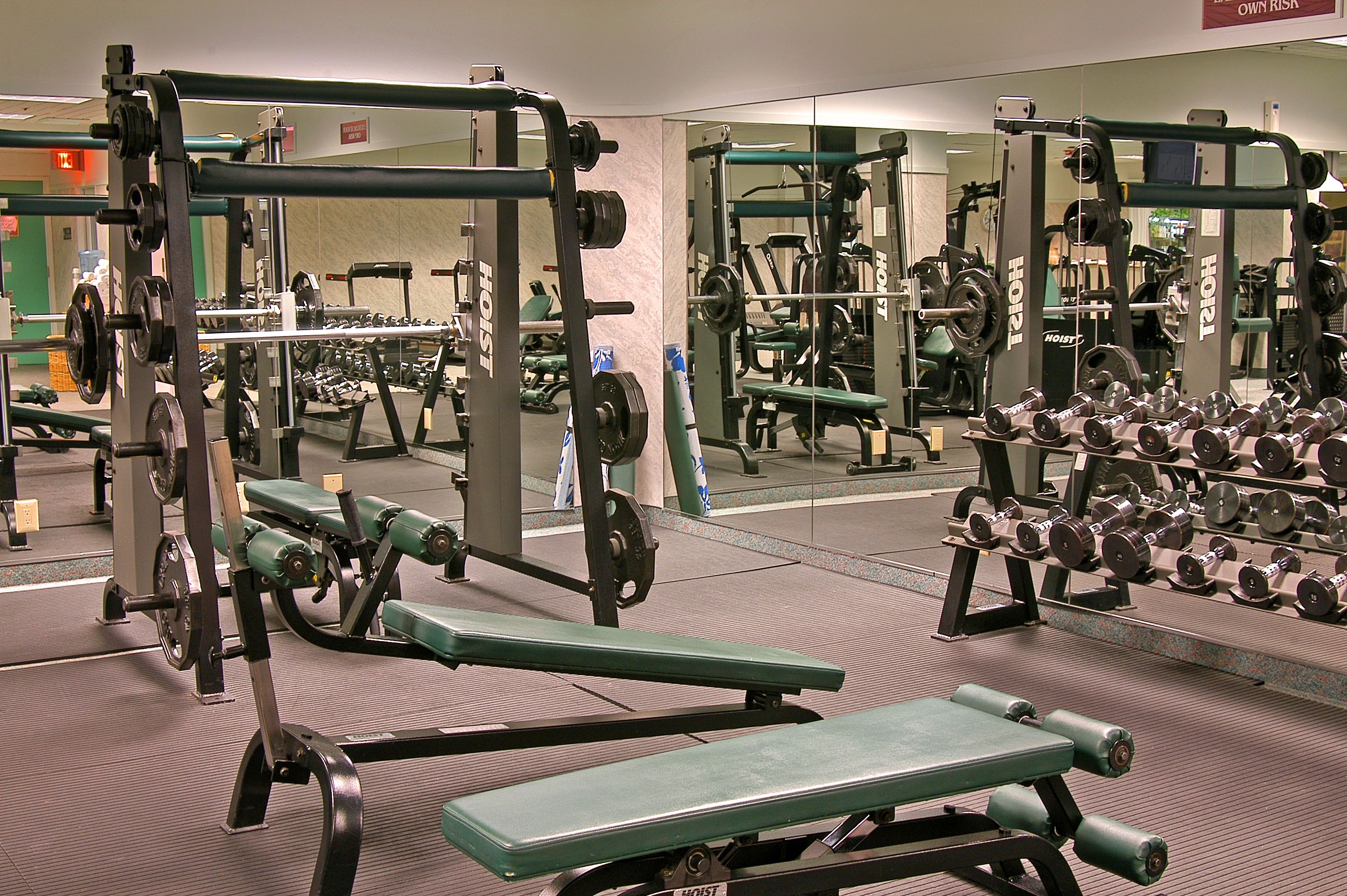 A gym with weightlifting equipment, benches, and mirrors.