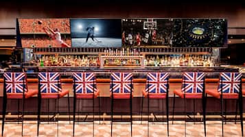 A bar with multiple screens displaying sports events, a variety of liquor bottles, and bar stools with Union Jack designs.