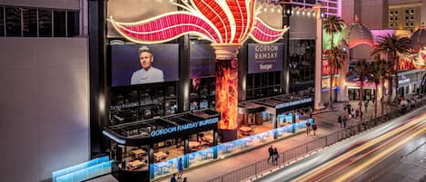 Ein Gordon Ramsay Burger Restaurant mit einer großen, beleuchteten Schautafel, Außenbereich und Blick auf die Straße.
