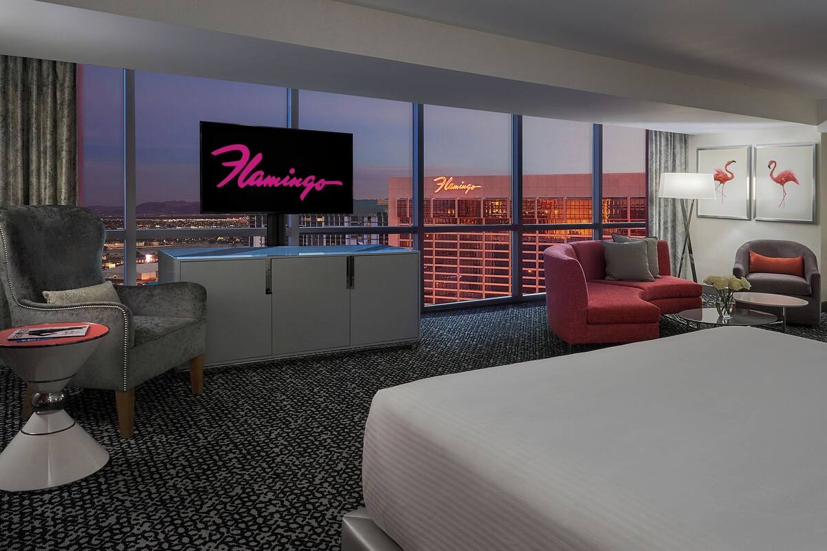 A hotel room with a large window, a flat-screen TV, a bed, a desk, and a chair.